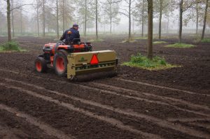 Meneer op machine grondbewerking onder bomen
